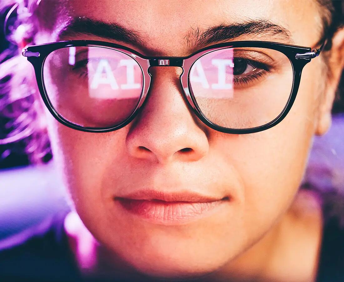 Woman wearing glasses that are reflecting the word "AI"