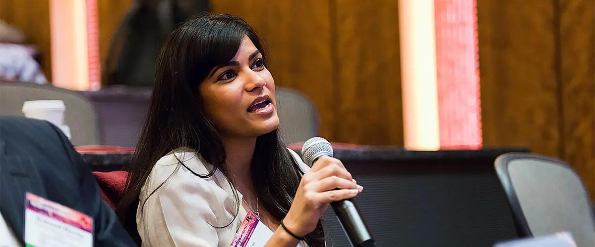 A woman with a microphone asking a question at a symposium event.